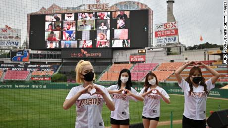Cheerleaders pose in front of a large screen featuring baseball fans cheering from their homes during the opening match of South Korea's new baseball season between SK Wyvern and Hanwha Eagles at Munhak Baseball Stadium in Incheon on Tuesday.