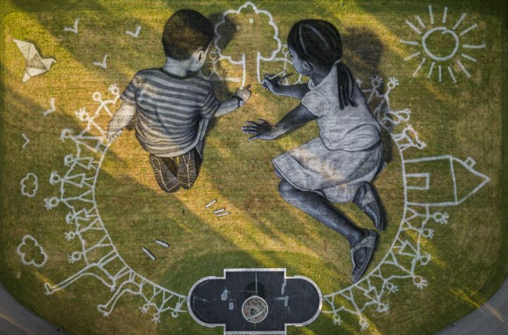 In this picture made available Friday, June 26, 2020 an aerial view shows a giant ephemeral landart painting by Swiss French artist Saype entitled "World in Progress" representing two children drawing their ideal world, at the European headquarters of the United Nations in Geneva, Switzerland, Wednesday, June 24, 2020. The artwork covering 6000 square meters was produced with biodegradable paints made from natural pigments such as coal and chalk. The fresco, offered by Switzerland, for the the 75th anniversary of the signing of the United Nations Charter in San Francisco on 26.6.1945 will be inaugurated by Swiss Federal Councillor Ignazio Cassis, in the presence of the Director-General of the United Nations Office in Geneva, Tatiana Valovaya. (Valentin Flauraud/Keystone via AP)