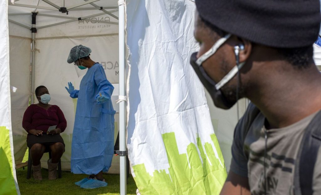 FILE — In this May 8, 2020, file photo a man looks into a tent as a health worker in protective gear collects a sample for COVID-19 testing in Diepsloot, Johannesburg, South Africa. South Africa’s reported coronavirus are surging. Its hospitals are now bracing for an onslaught of patients, setting up temporary wards and hoping advances in treatment will help the country’s health facilities from becoming overwhelmed. (AP Photo/Themba Hadebe, File)