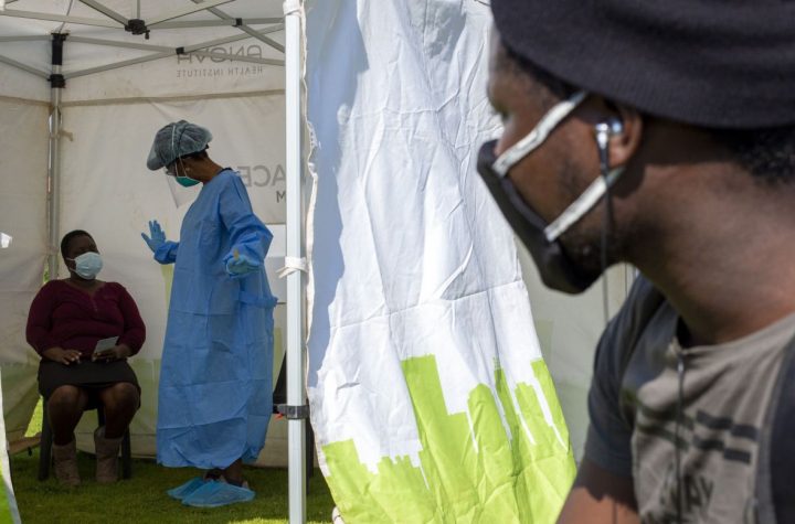 FILE — In this May 8, 2020, file photo a man looks into a tent as a health worker in protective gear collects a sample for COVID-19 testing in Diepsloot, Johannesburg, South Africa. South Africa’s reported coronavirus are surging. Its hospitals are now bracing for an onslaught of patients, setting up temporary wards and hoping advances in treatment will help the country’s health facilities from becoming overwhelmed. (AP Photo/Themba Hadebe, File)