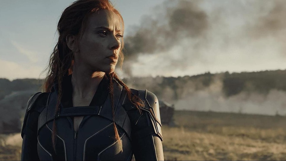 A woman dressed as a superhero looks at the horizon.  Black smoke appears in the background.