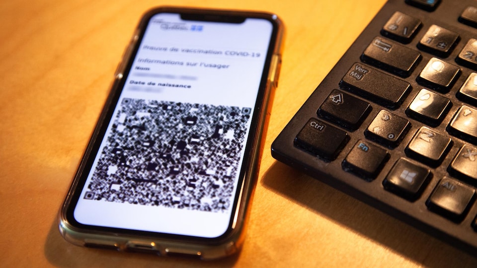 A vaccine-proof cell phone from the Quebec government is placed on a table next to a working keyboard.