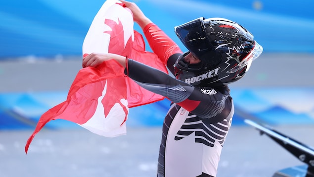 Une athlète fait flotter le drapeau canadien dans les airs après avoir gagné une médaille.