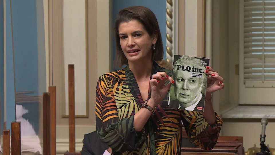 Genevieve Gilbolt, standing in the assembly, holds a book with Jean Charrest on the cover.