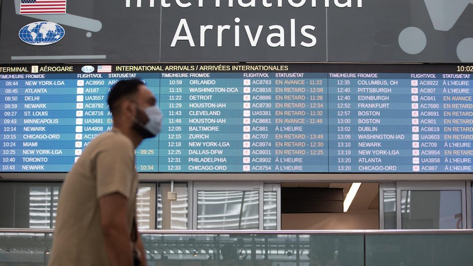 A masked man walks in front of an electronic board displaying aircraft at Toronto's Pearson Airport.