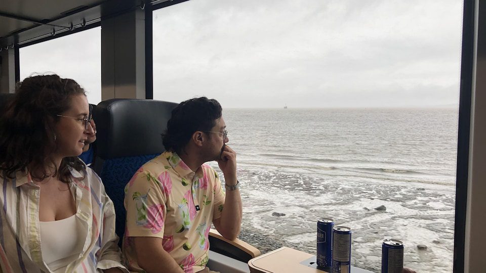 Two men look out the window of a huge train at the St. Lawrence River. 