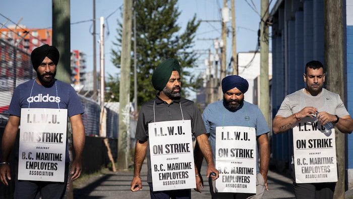 Four Port of Vancouver employees march with signs on July 19, 2023.