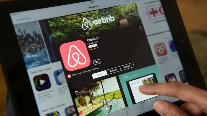 A finger is about to tap the download button of the Airbnb application on a tablet. 