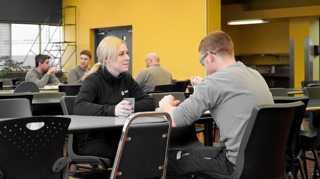 A woman sits across from a man at a table in a cafeteria. 