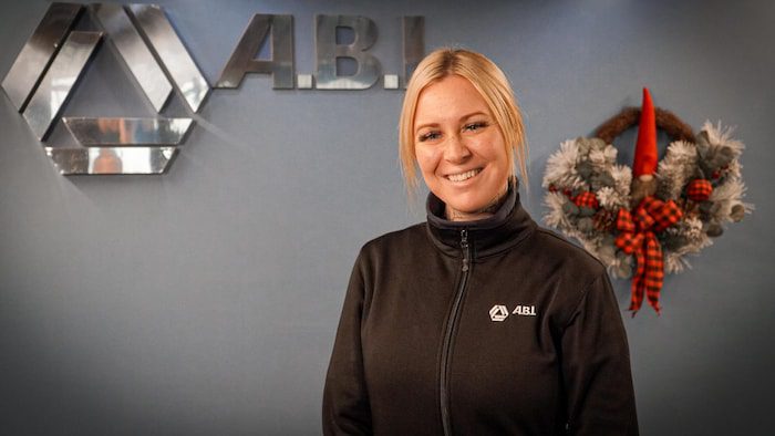 Smiling woman standing in front of wall with ABI company logo.