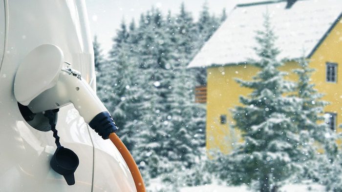 An electric car connected to a charging cable.  It is winter.