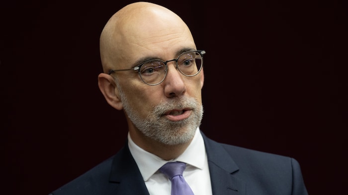 A man wears a jacket, tie and glasses.